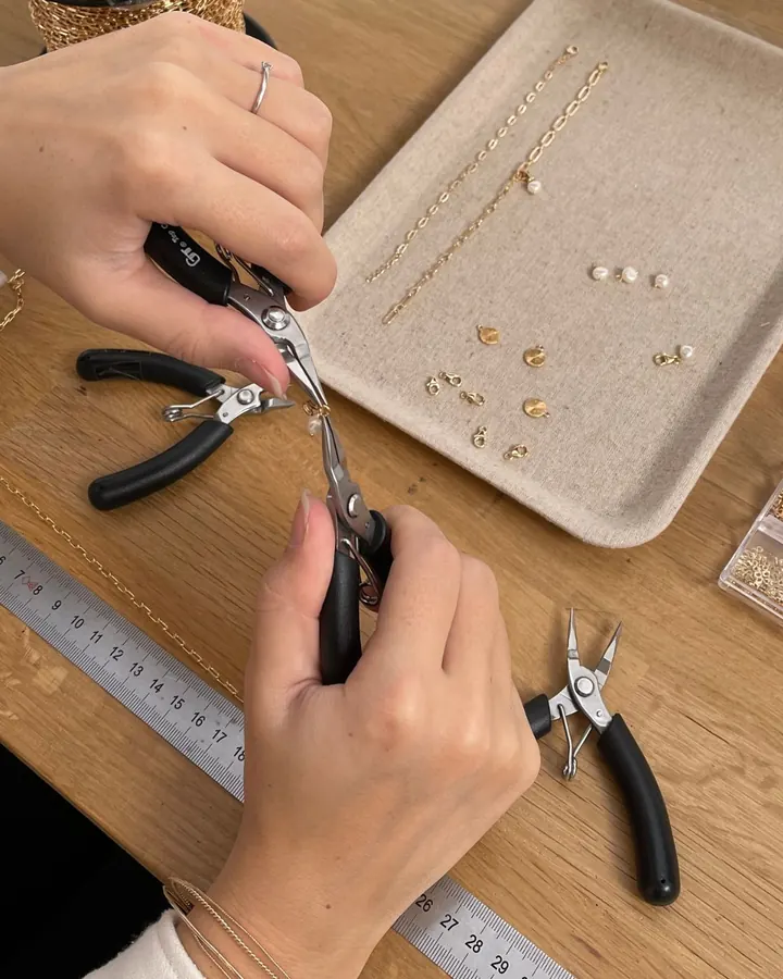 Mains montant un bijou à la pince dans l'atelier Instants Plaisirs